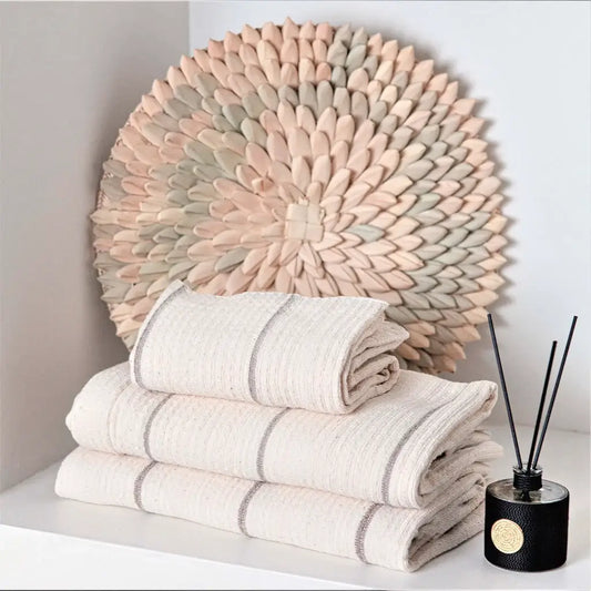 Stack of white towels with gray stripes on a white surface, with a porcupine wall piece and diffuser in the background.