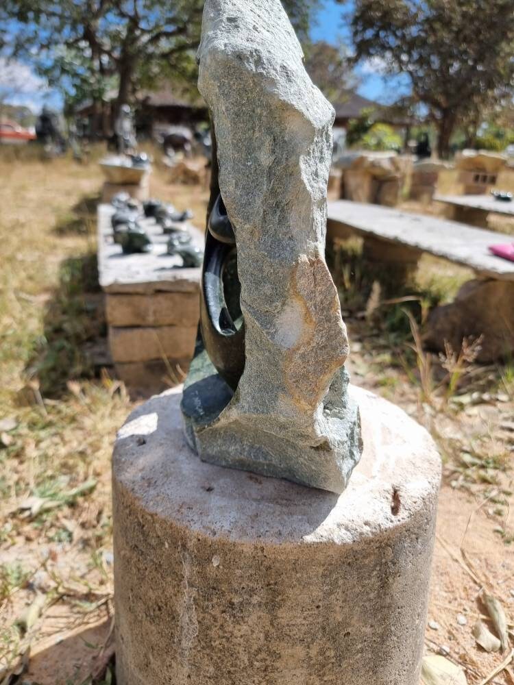 Shona Stone sculpture of a figure on a pedestal outdoors with blurred background