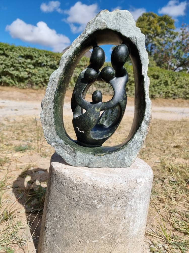 Abstract sculpture of people in a circle on a stone base outdoors