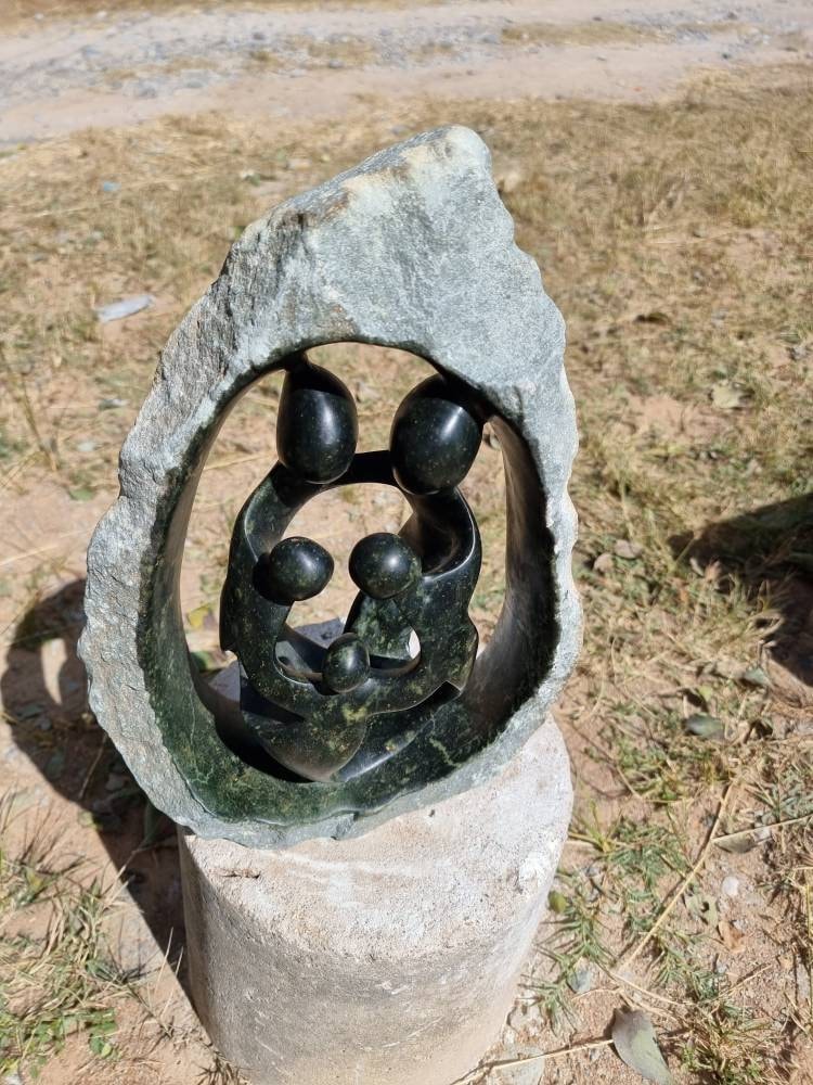 Shona stone sculpture of abstract figures in a circular design outdoors.